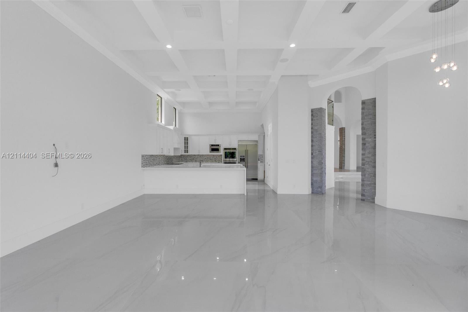 Coffered ceiling, polished stone-finish flooring, built-in kitchen cabinetry with integrated appliances, and gray stone-finish columns
