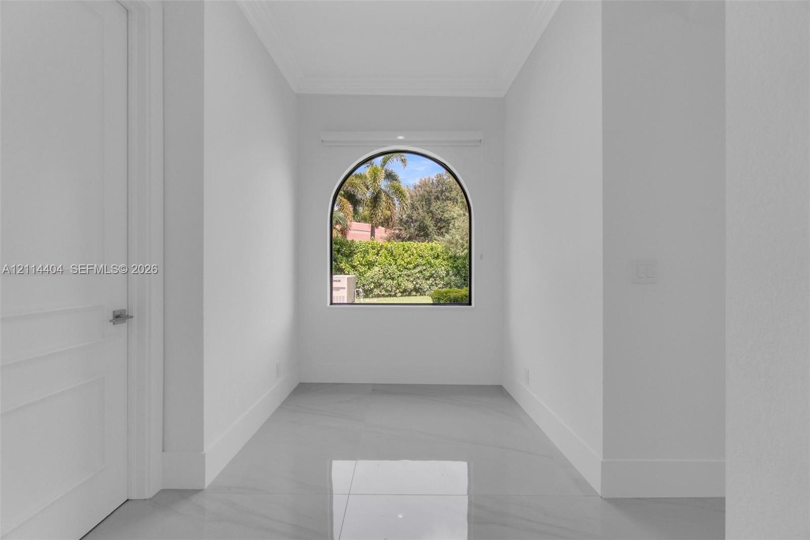 Arched window with black frame, neutral wall finishes, and polished tile flooring