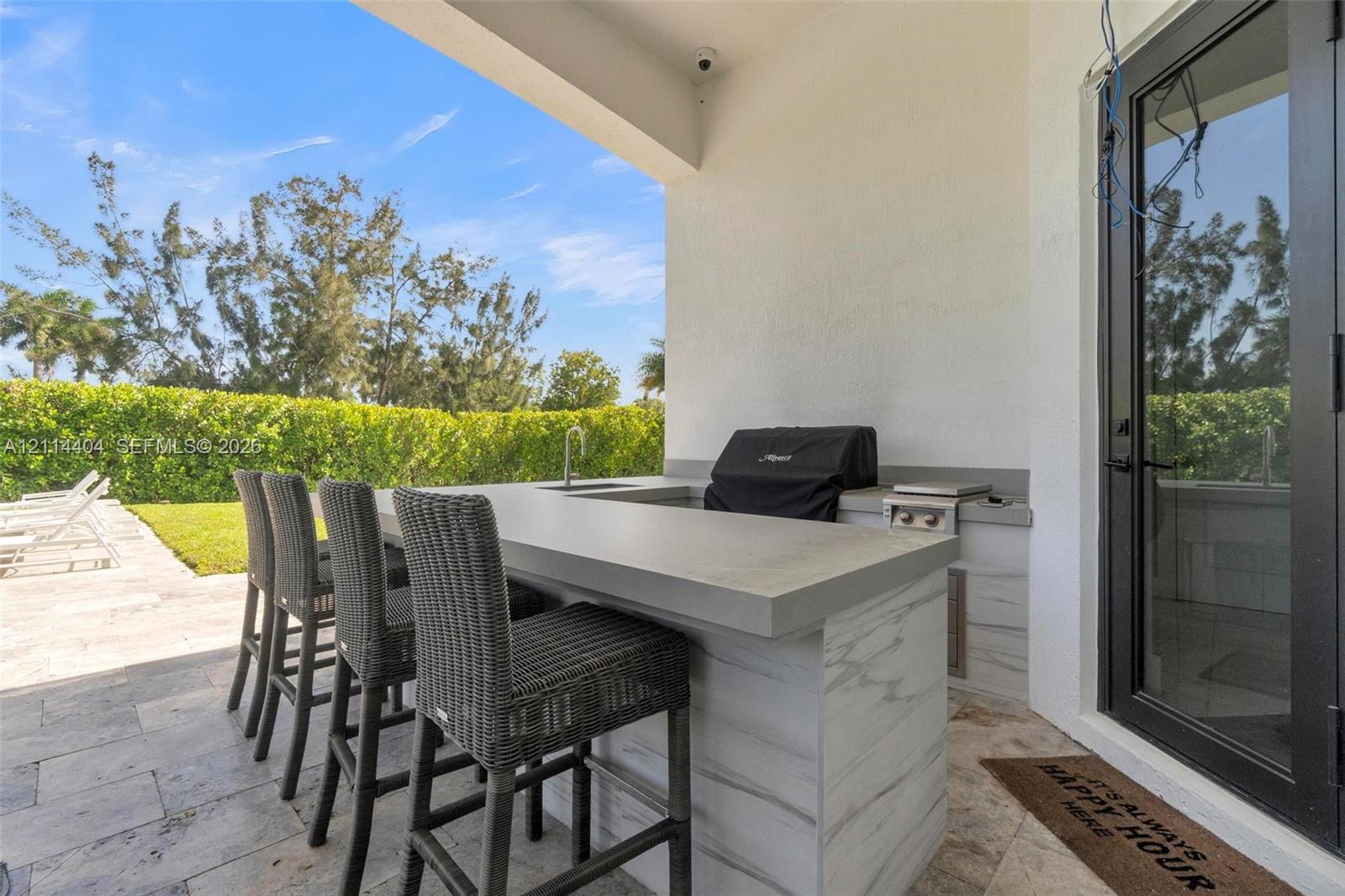 Covered outdoor kitchen featuring stone-finish flooring, a built-in grill, a sink, and a bar-height counter with decorative surfacing