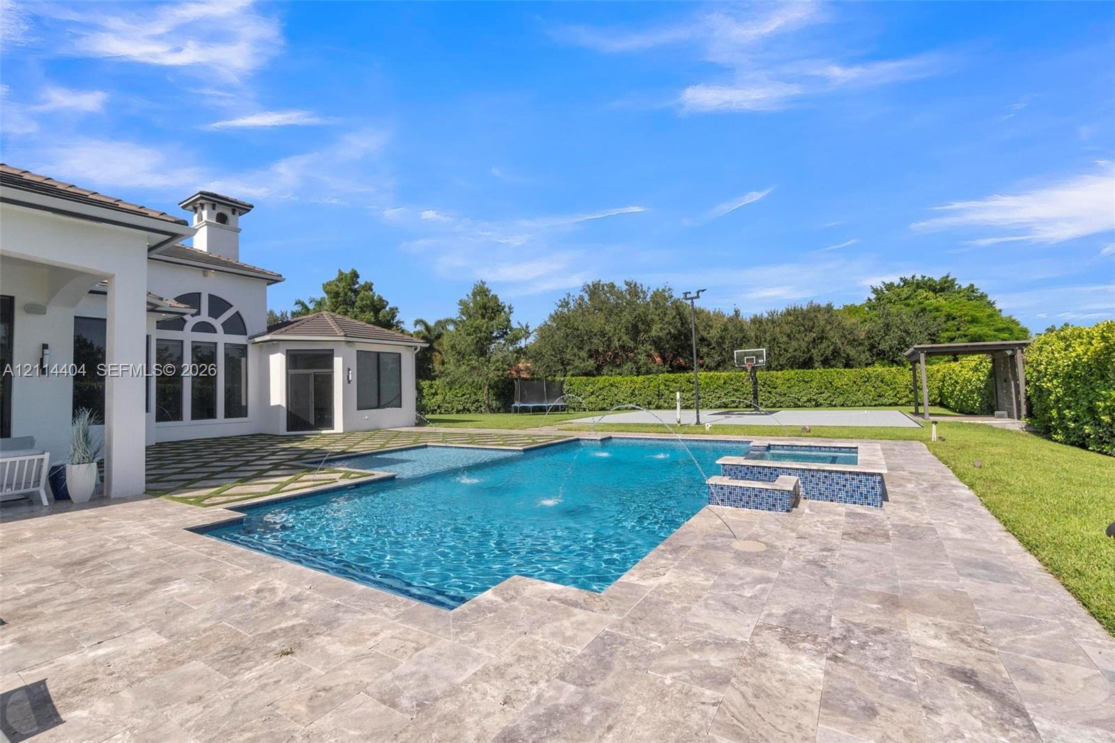 Backyard featuring an inground pool with water features, integrated spa, stone paver decking, and a sport court