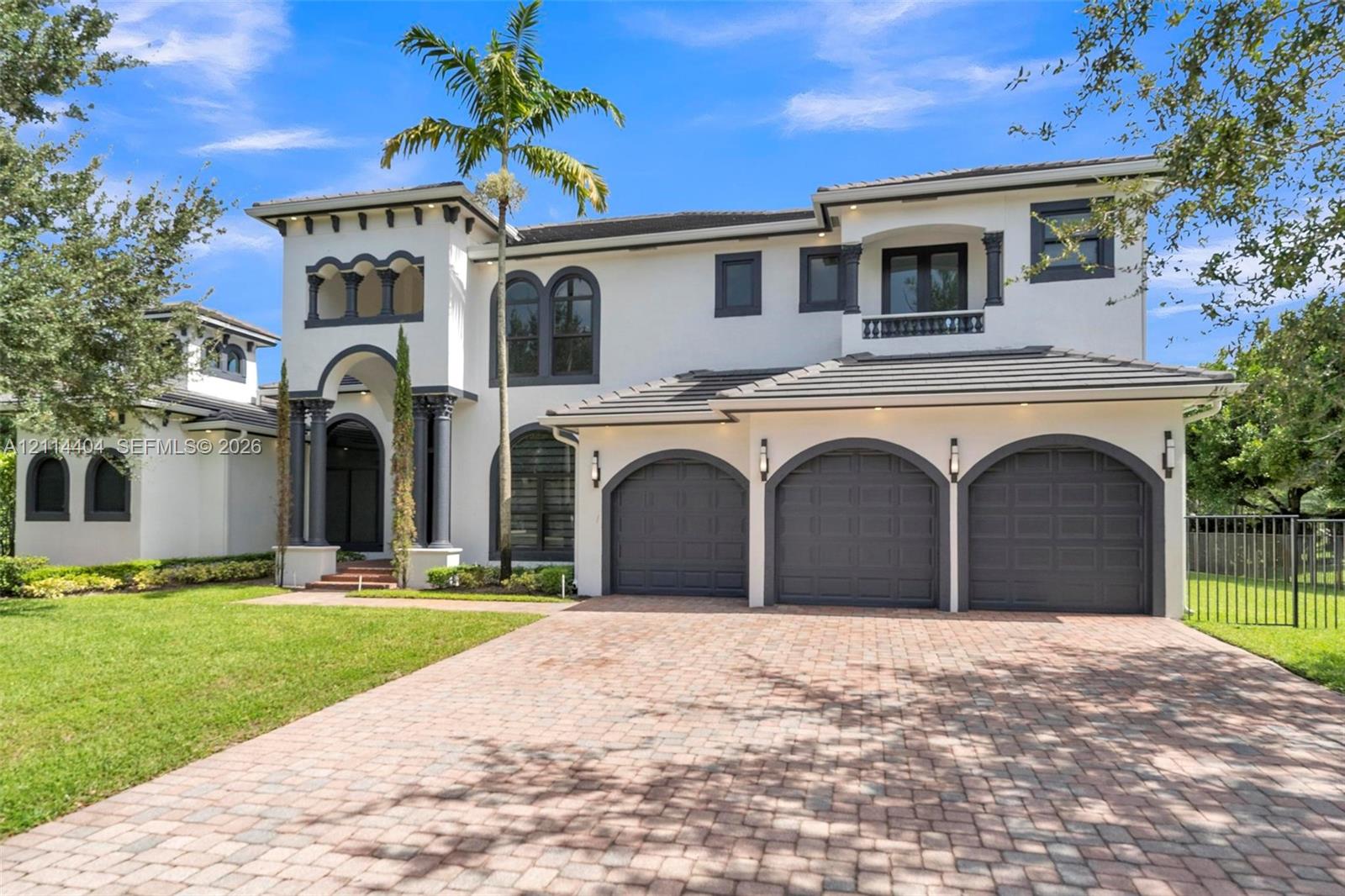Mediterranean-style exterior featuring smooth stucco finish, arched entryway with decorative columns, three-car garage with arched doors, second-level balcony, and brick-paver driveway Mediterranean-style exterior featuring smooth stucco finish, arched entryway with decorative columns, three-car garage with arched doors, second-level balcony, and brick-paver driveway