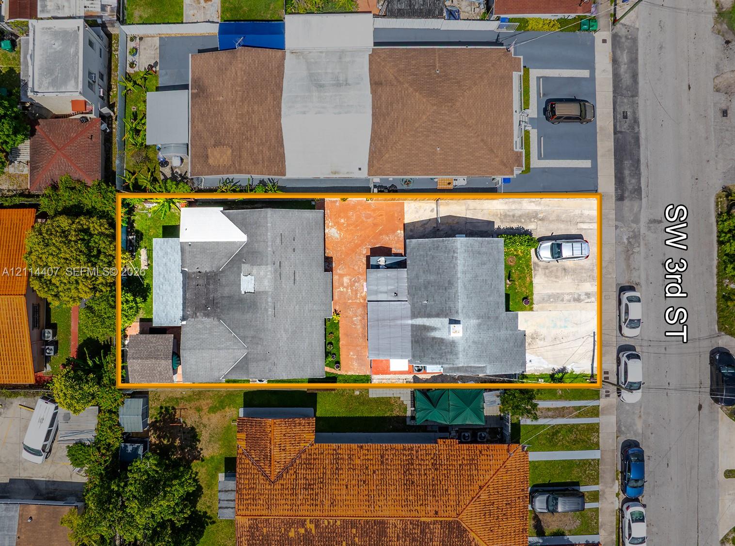 Aerial view of a rectangular lot featuring two structural footprints, concrete paving, and perimeter fencing