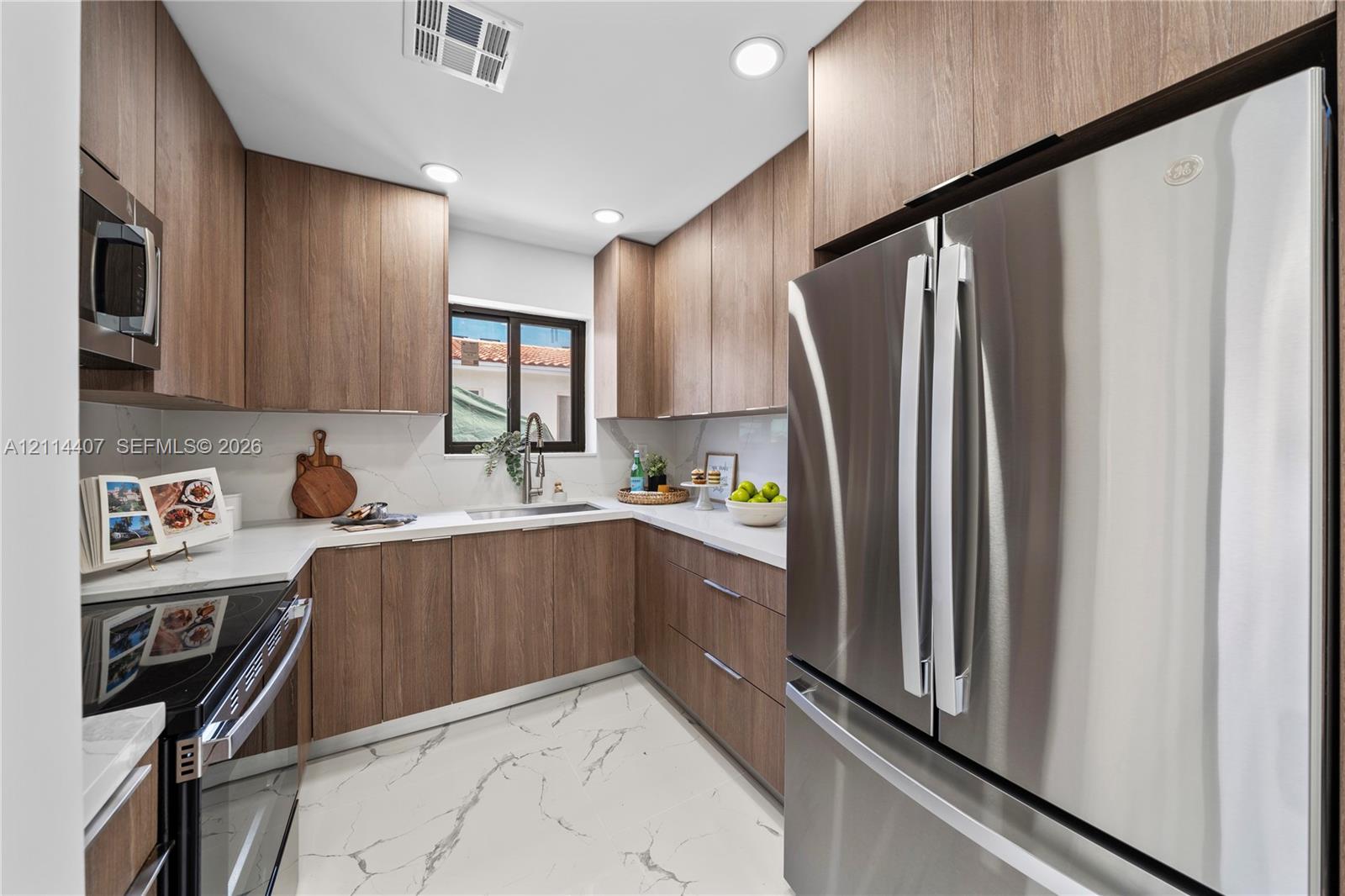 Kitchen featuring wood-finish cabinetry, white countertops, full-height stone-patterned backsplash, stainless steel appliances, and large-format tile flooring