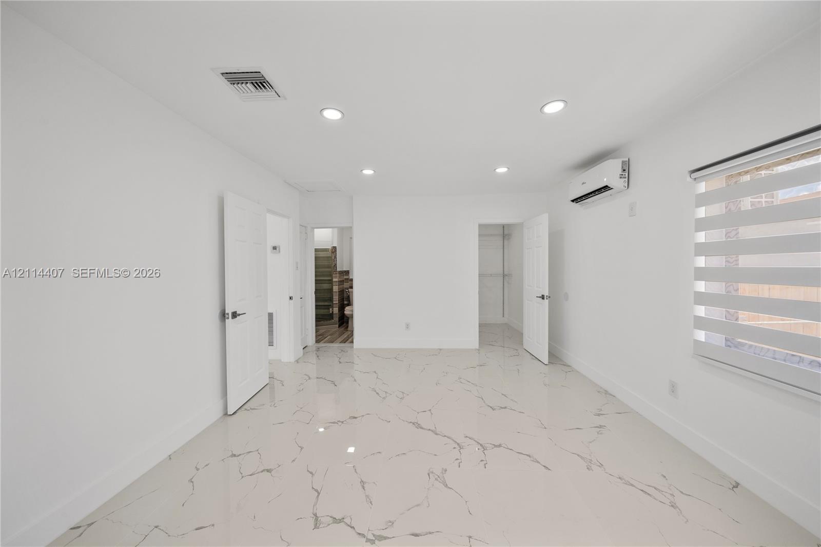 Large-format tile flooring with veining detail, recessed ceiling lighting, wall-mounted ductless air conditioning unit, and built-in closet storage