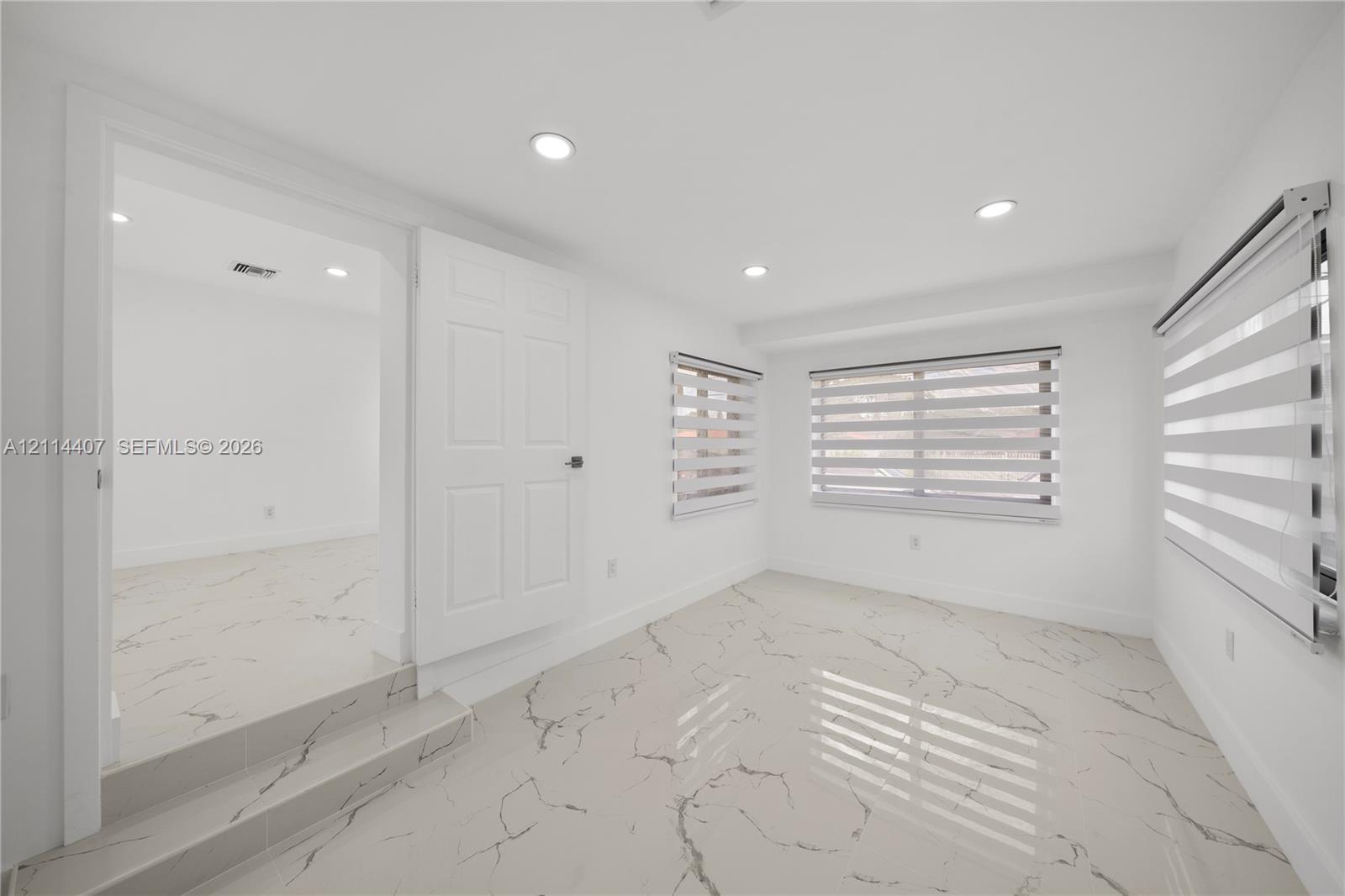Interior space featuring stone-style tile flooring with veining, recessed lighting, multi-panel doors, and horizontal zebra-style window treatments