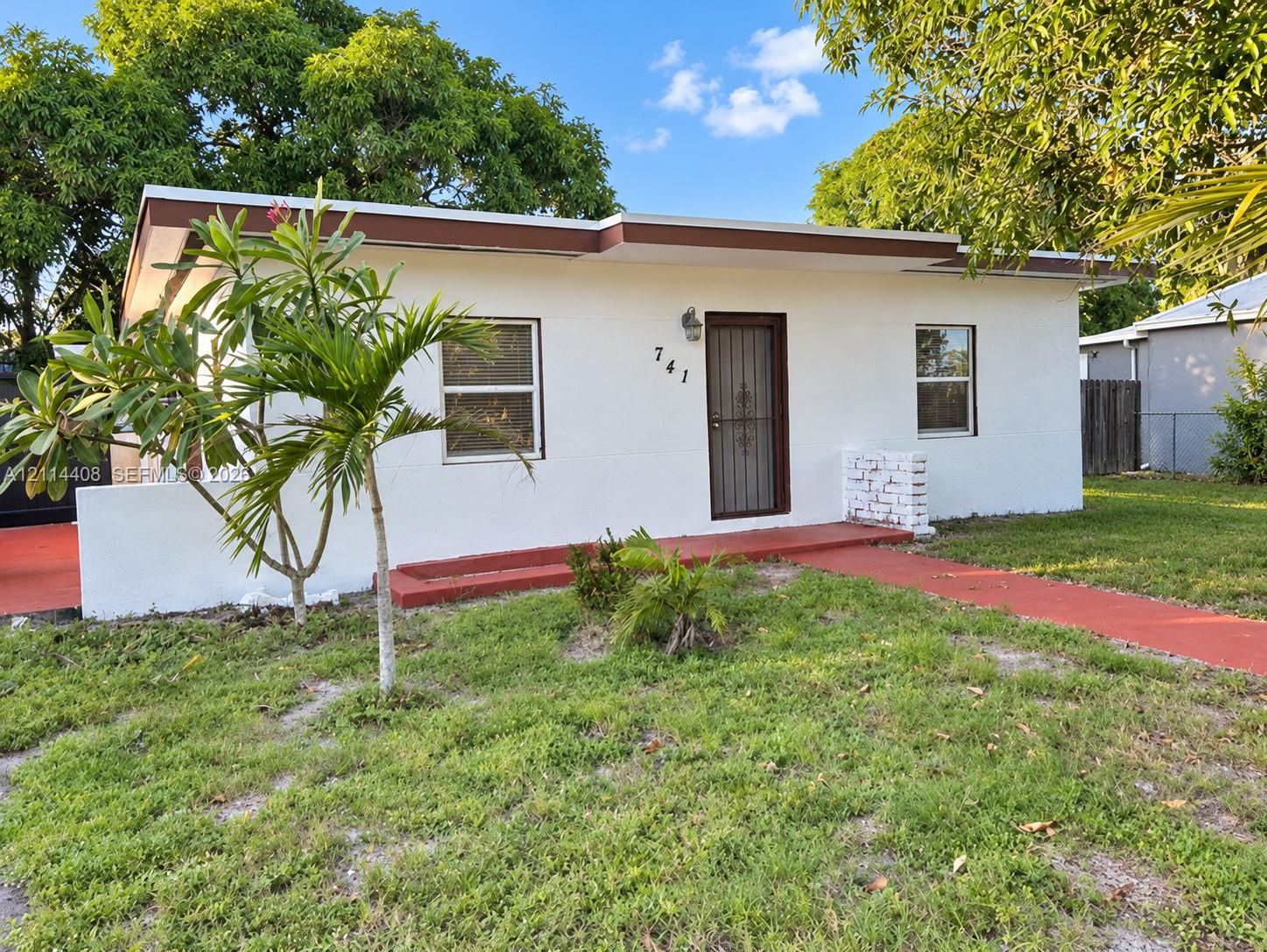 Single-story exterior featuring white stucco finish, flat roofline, metal-framed windows, and a paved entrance walkway Single-story exterior featuring white stucco finish, flat roofline, metal-framed windows, and a paved entrance walkway