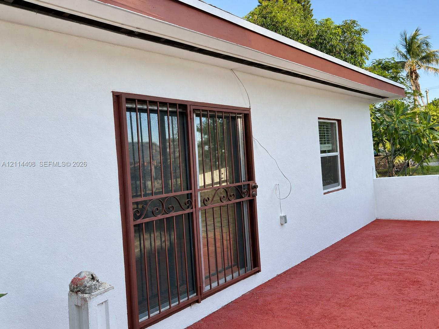 Exterior elevation featuring stucco siding, sliding glass doors with metal security bars, single-hung window, and painted concrete patio
