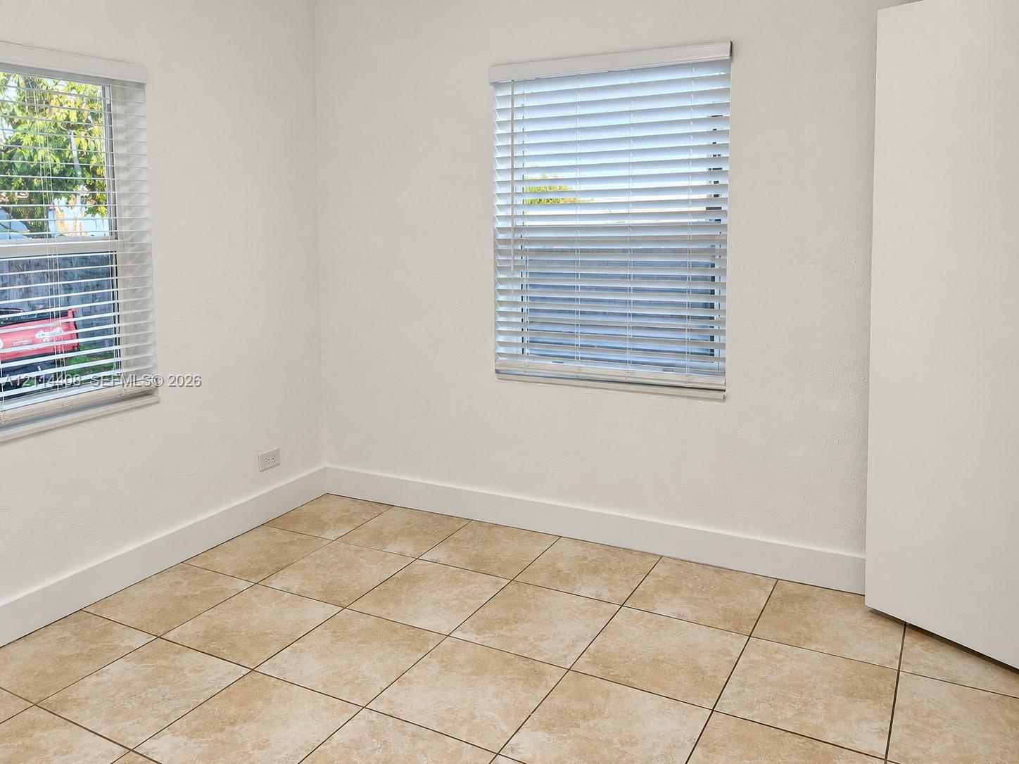 Neutral interior featuring light-colored tile flooring, smooth wall finishes, and two windows equipped with horizontal blinds