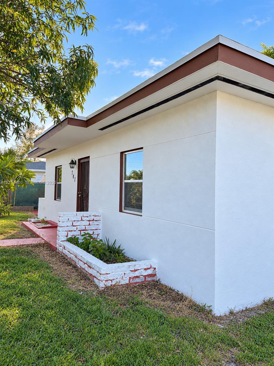 Stucco exterior featuring flat roof lines, deep roof overhangs, a painted brick planter, and a metal security screen door