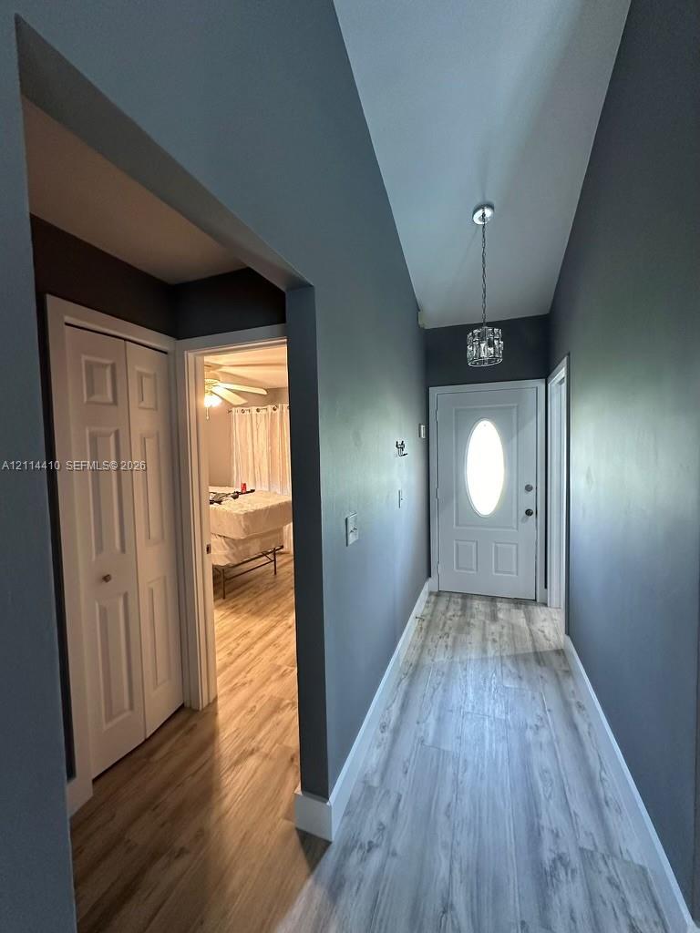 Entryway featuring wood-finish flooring, a white six-panel door with an oval glass insert, bi-fold closet doors, and a crystal-accented pendant light fixture