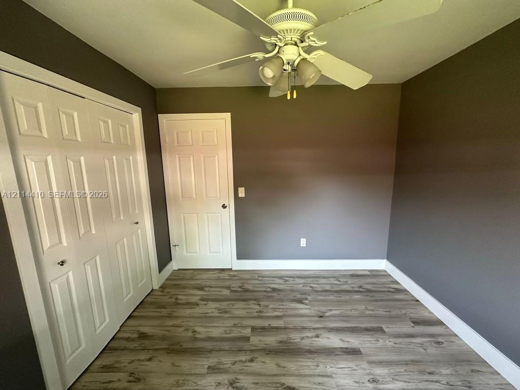 Wood-finish flooring, white paneled closet doors, six-panel interior door, and a ceiling-mounted light fixture with a fan