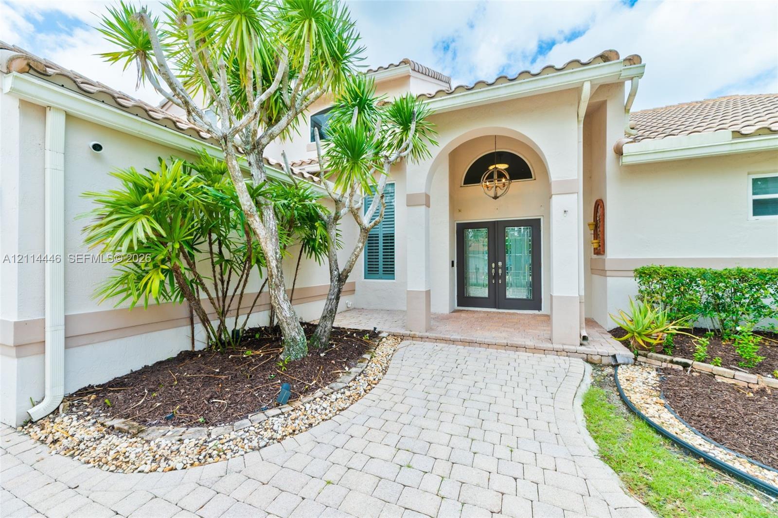 Stucco exterior featuring a covered entryway with an arched porch, double glass-paneled front doors, a tiled roof, and a paved walkway