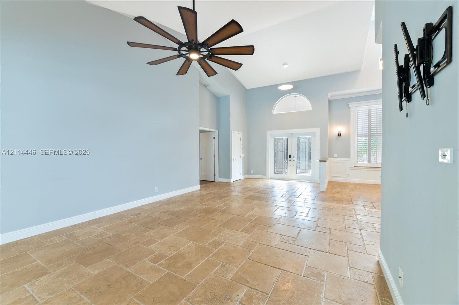 Vaulted ceilings, large-format tile flooring, multi-blade ceiling fan, arched window, and double glass entry doors