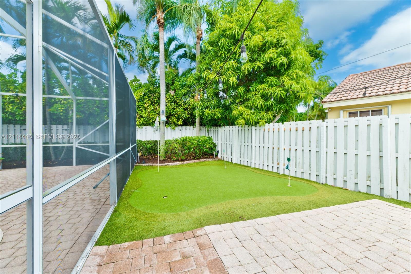 Backyard featuring a synthetic putting green, paver patio, full-height privacy fencing, and a screened enclosure