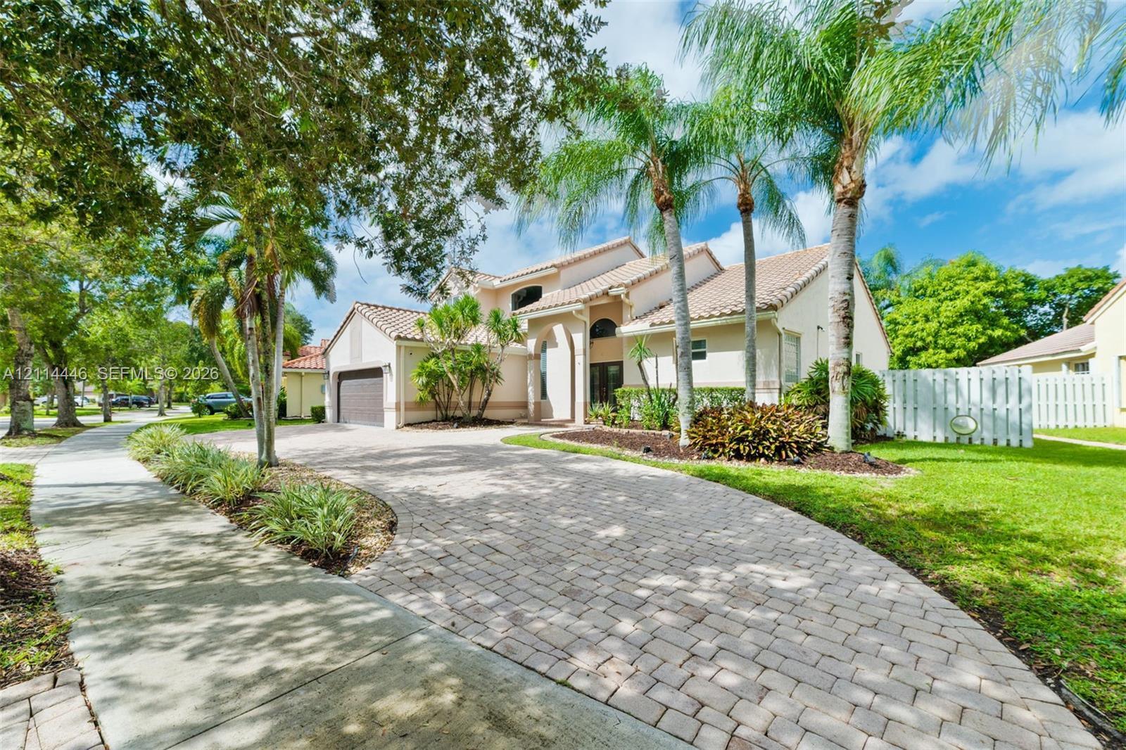 Stucco exterior featuring a tile roof, arched entryway, brick-paver driveway, and mature palm landscaping