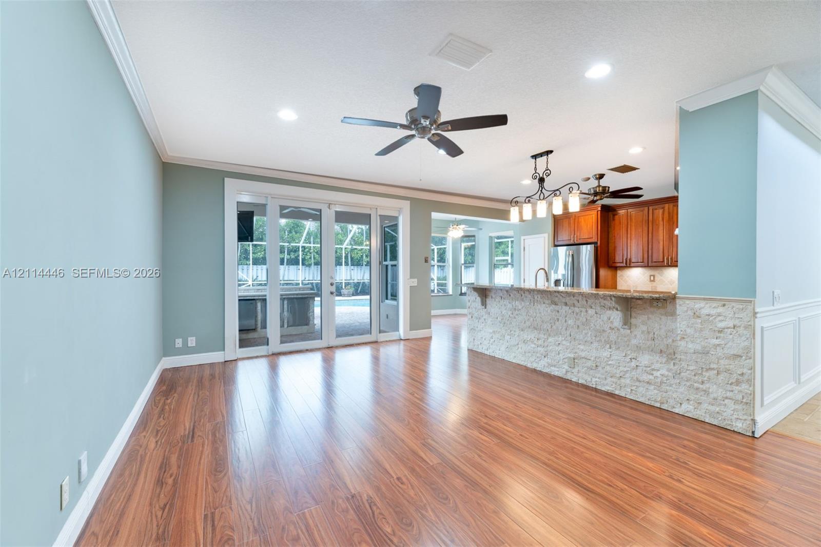 Open-concept area featuring wood-finish flooring, a tiered breakfast bar with stone-veneer facing, recessed lighting, ceiling fans, and multi-panel glass doors