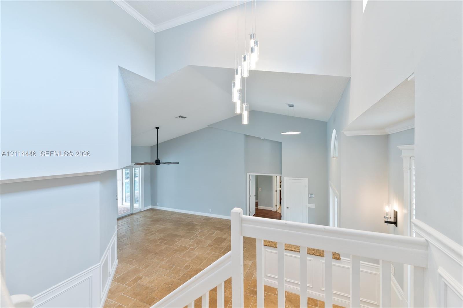 Vaulted ceilings with multi-pendant lighting, tile flooring, white wainscoting, and a white baluster railing