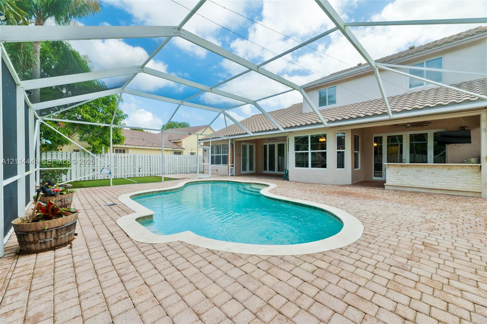 Screen-enclosed patio with a paver deck, built-in outdoor bar, and a freeform swimming pool