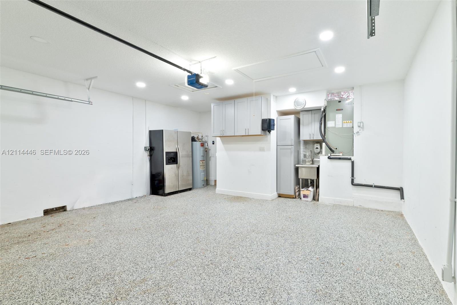 Garage space featuring an epoxy-coated floor, recessed lighting, built-in storage cabinetry, and a dedicated utility sink area