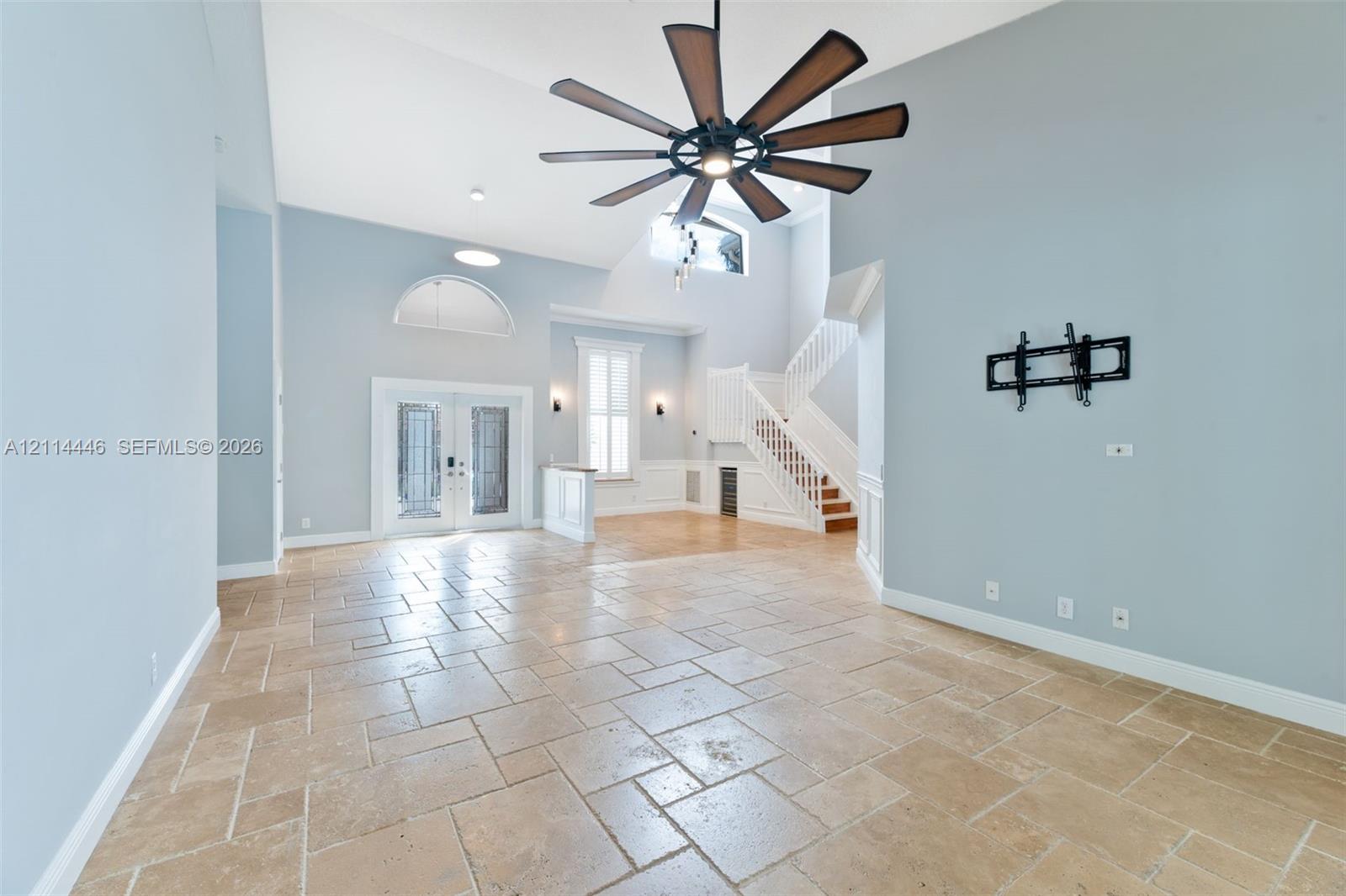 Open-concept space featuring high vaulted ceilings, large-format stone tile flooring, a multi-blade ceiling fan, arched window detailing, and a white staircase with wooden treads