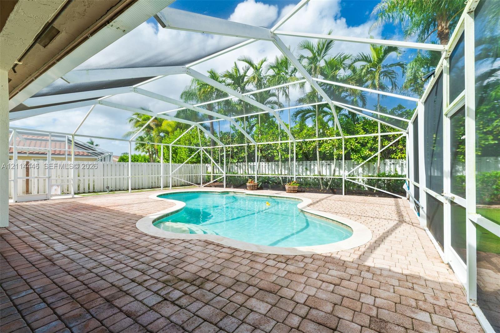 Screened-in patio featuring a paver-stone deck, freeform swimming pool, and white aluminum structural framing
