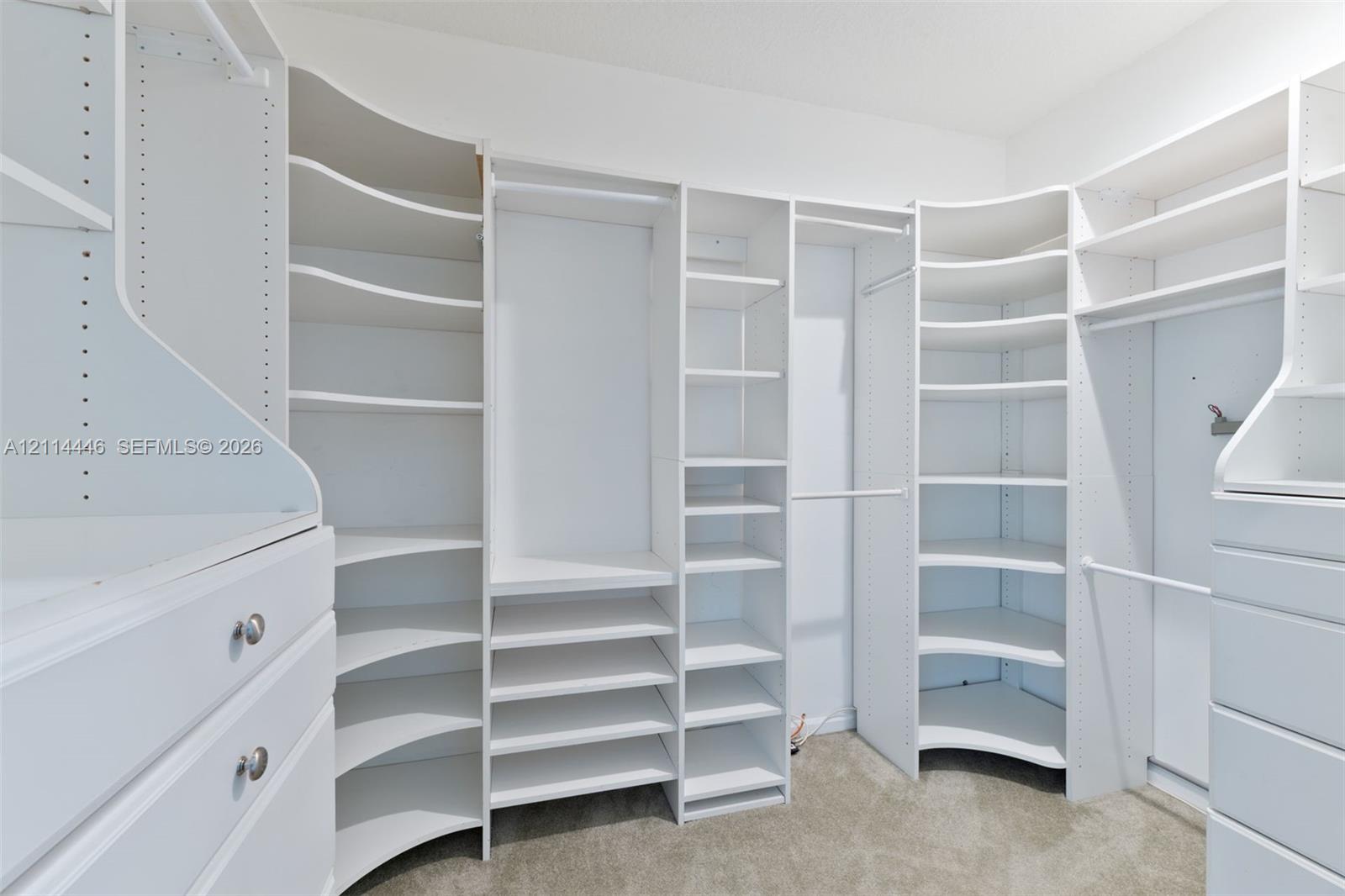 Walk-in closet featuring white built-in shelving, adjustable storage cubbies, curved corner shelves, and integrated drawers with metallic hardware