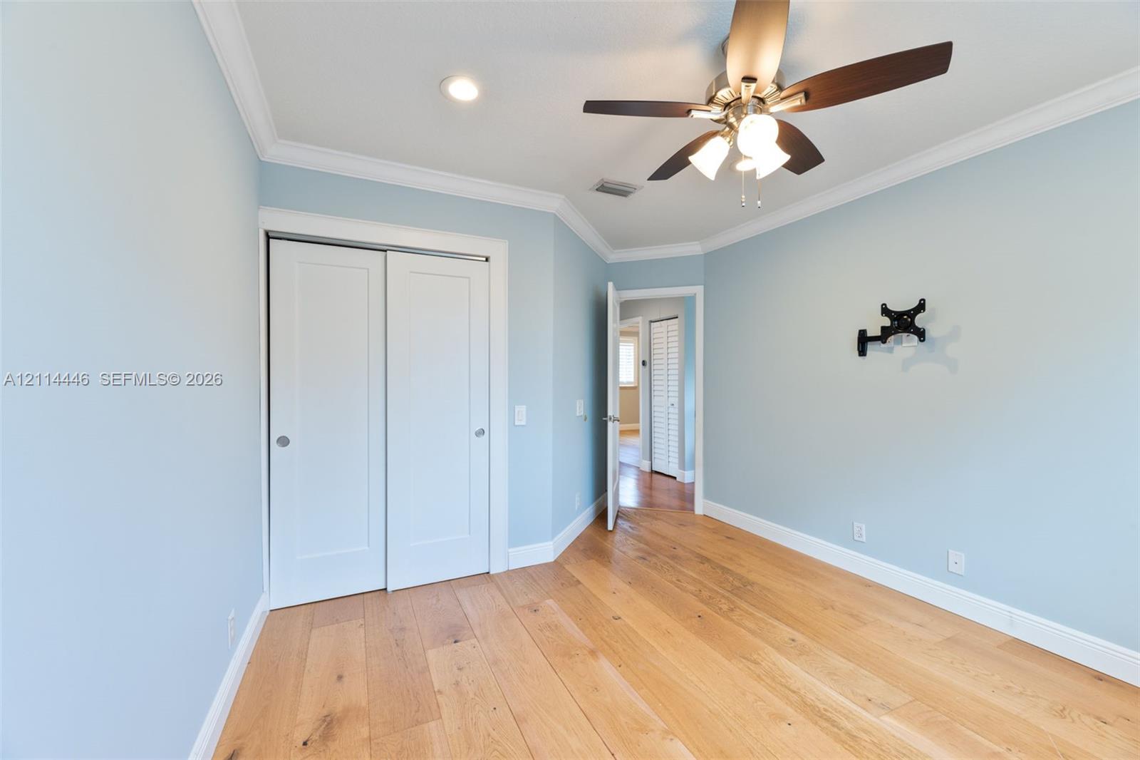 Room featuring light-toned wood-finish flooring, crown molding, double-panel closet doors, and a ceiling fan with integrated lighting