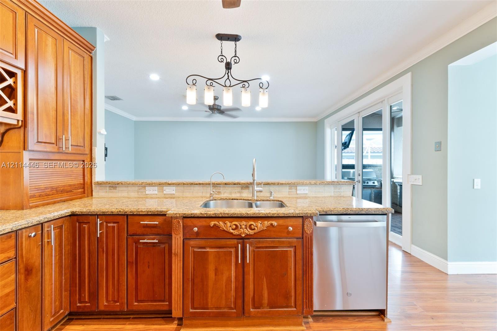 Kitchen featuring medium-toned wood cabinetry, stone countertops, stainless steel dishwasher, decorative carved wood detail, and a multi-light chandelier