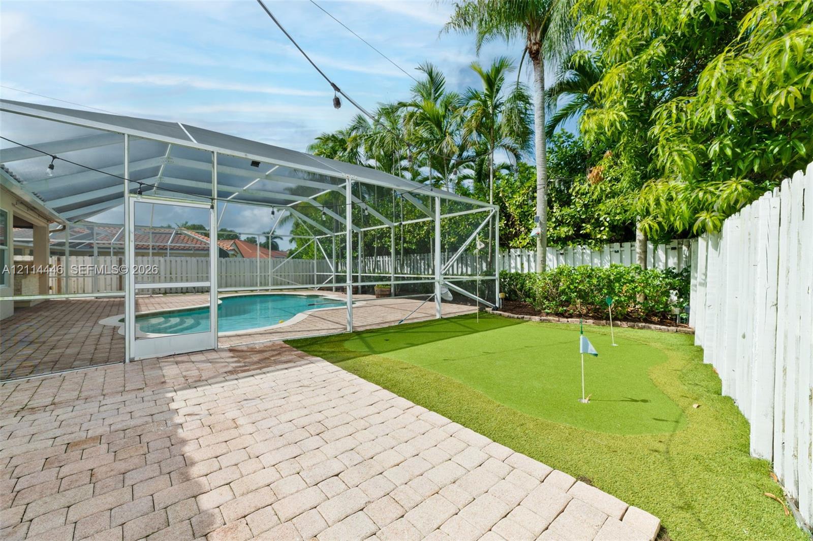 Screen-enclosed swimming pool, paver patio, integrated putting green, and perimeter wood fencing