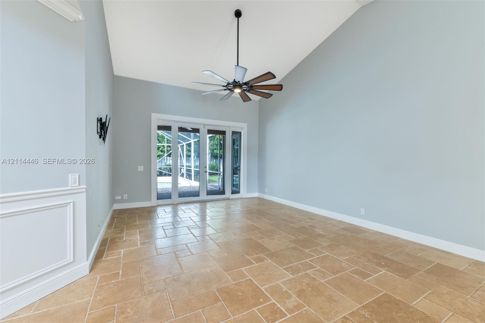 Vaulted ceilings featuring a multi-blade ceiling fan, stone-tile flooring, and glass-paneled exterior doors with an integrated screen enclosure