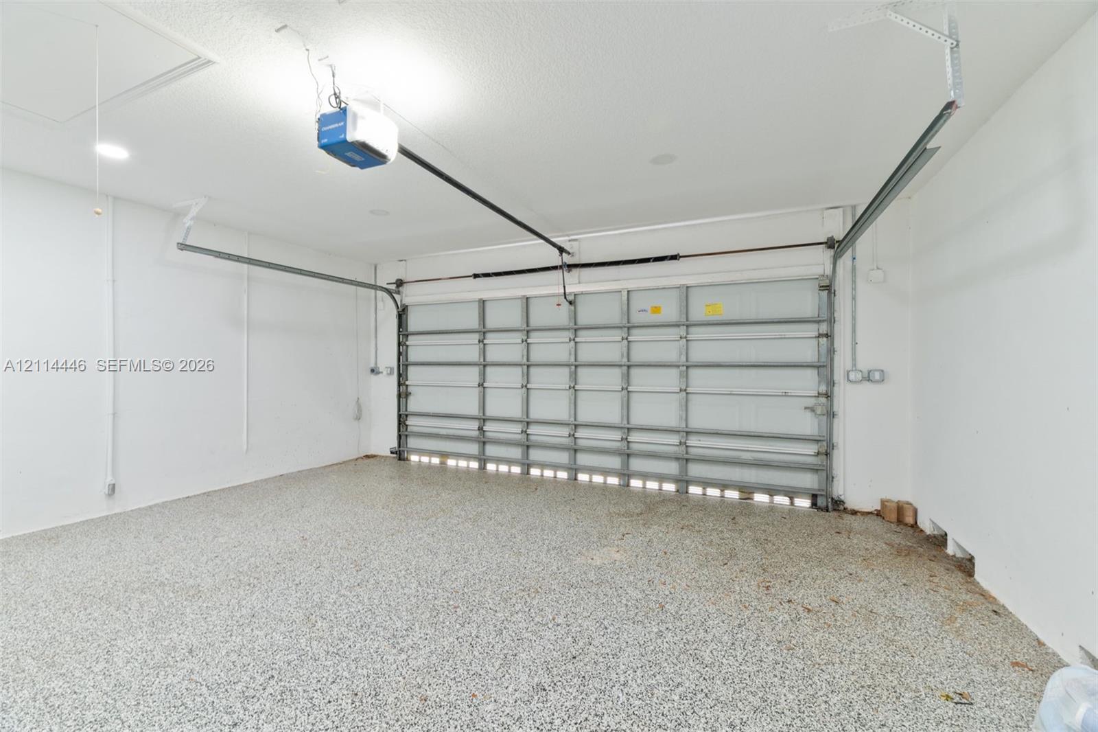 Two-car garage featuring epoxy-coated flooring, white interior walls, and an automated overhead door system