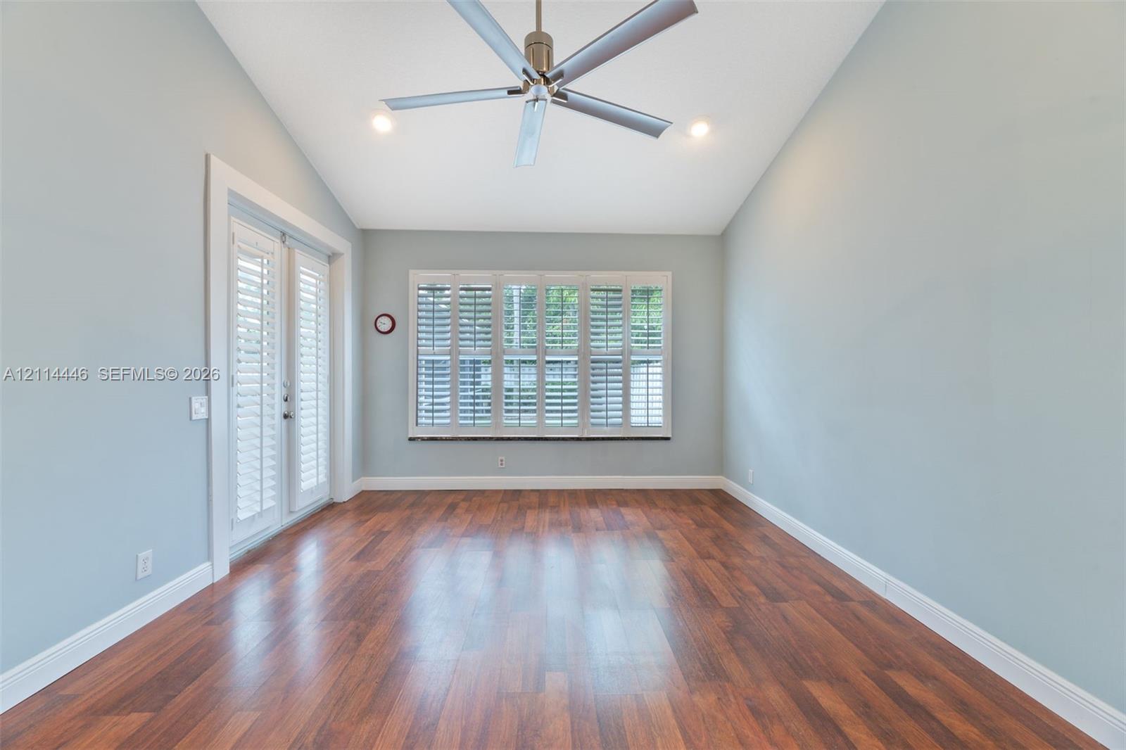 Vaulted ceiling room featuring wood-finish flooring, recessed lighting, a modern ceiling fan, plantation shutters, and glass-paneled double doors