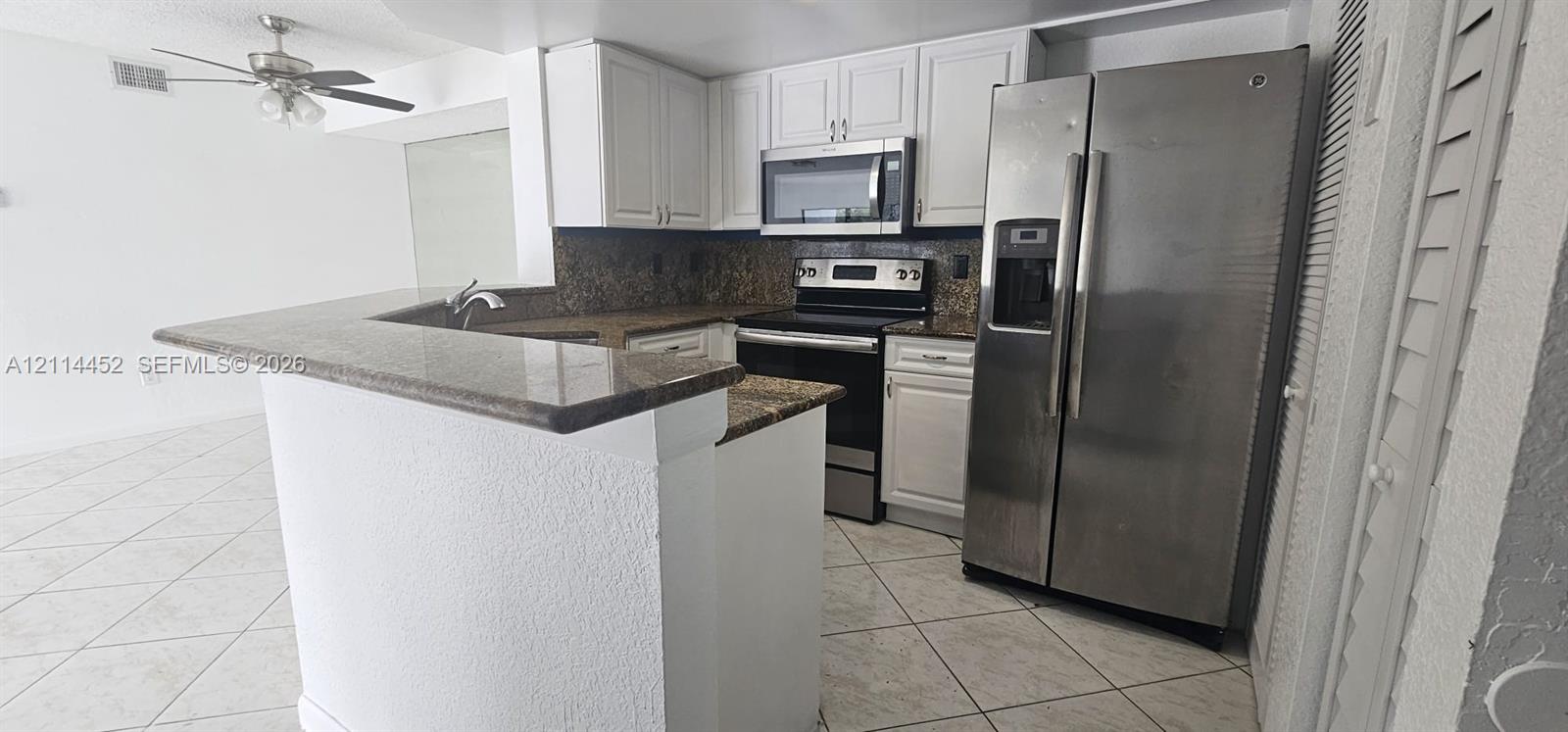 Kitchen featuring white shaker-style cabinetry, stone-finish countertops, stainless steel appliances, and tile flooring Kitchen featuring white shaker-style cabinetry, stone-finish countertops, stainless steel appliances, and tile flooring