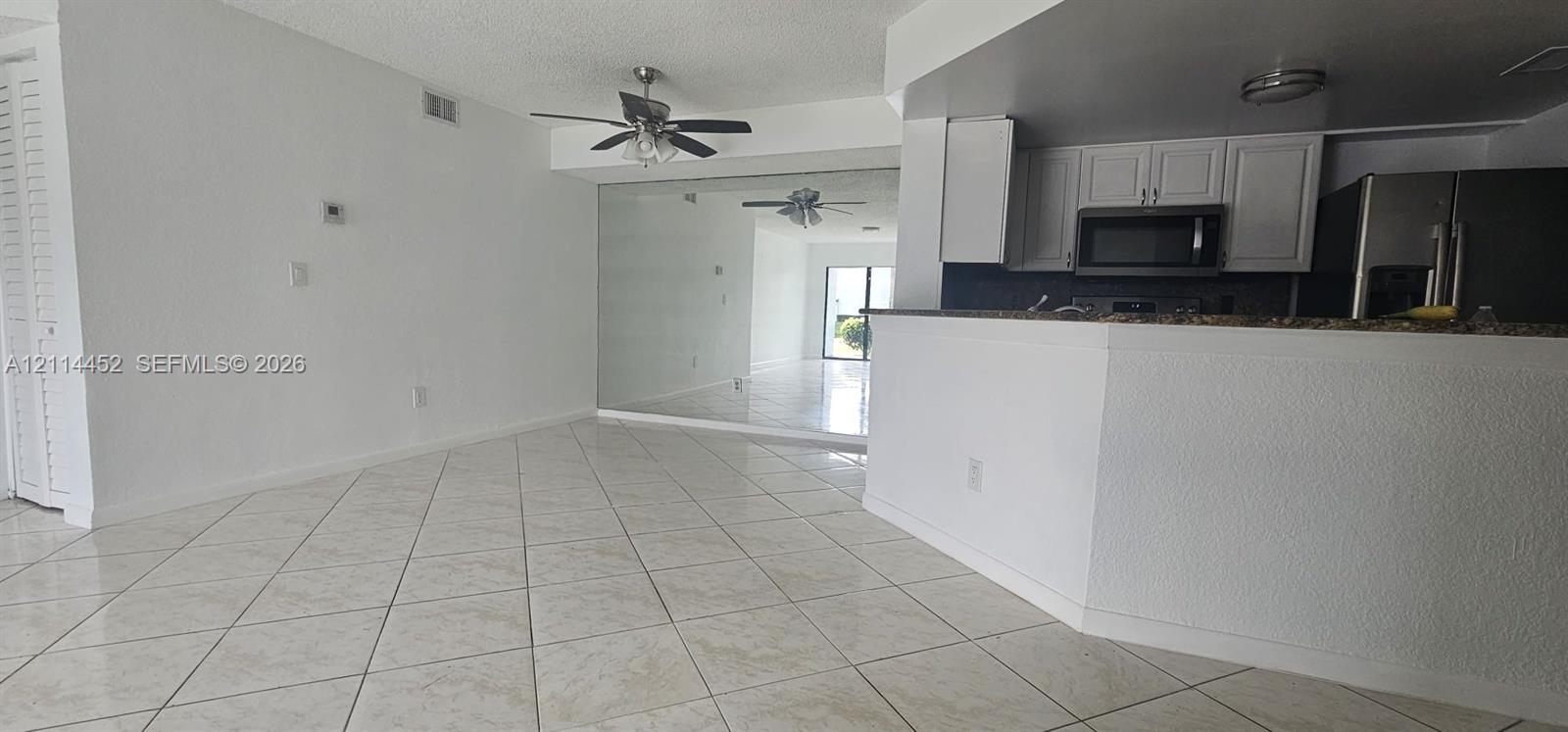 Open-concept interior featuring diagonal tile flooring, white cabinetry, dark stone-finish countertops, built-in ceiling fans, and a full-height wall mirror Open-concept interior featuring diagonal tile flooring, white cabinetry, dark stone-finish countertops, built-in ceiling fans, and a full-height wall mirror