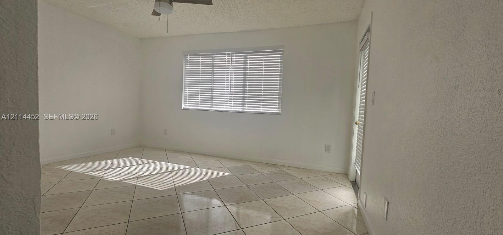 Room interior featuring large-format diagonal tile flooring, textured wall finish, and an integrated ceiling fan Room interior featuring large-format diagonal tile flooring, textured wall finish, and an integrated ceiling fan