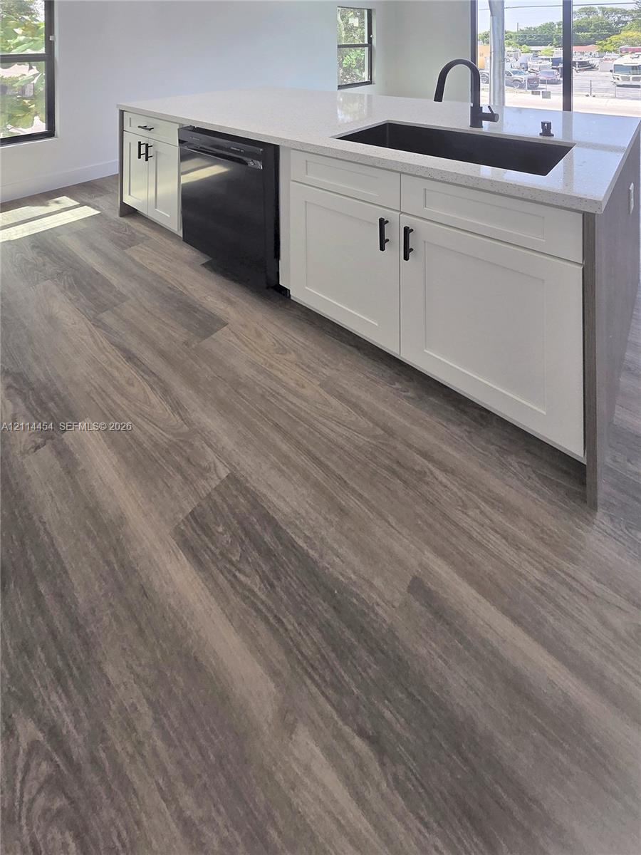 Kitchen island featuring white shaker-style cabinetry, matte black hardware, stone-composite countertop, undermount sink, and wood-finish flooring