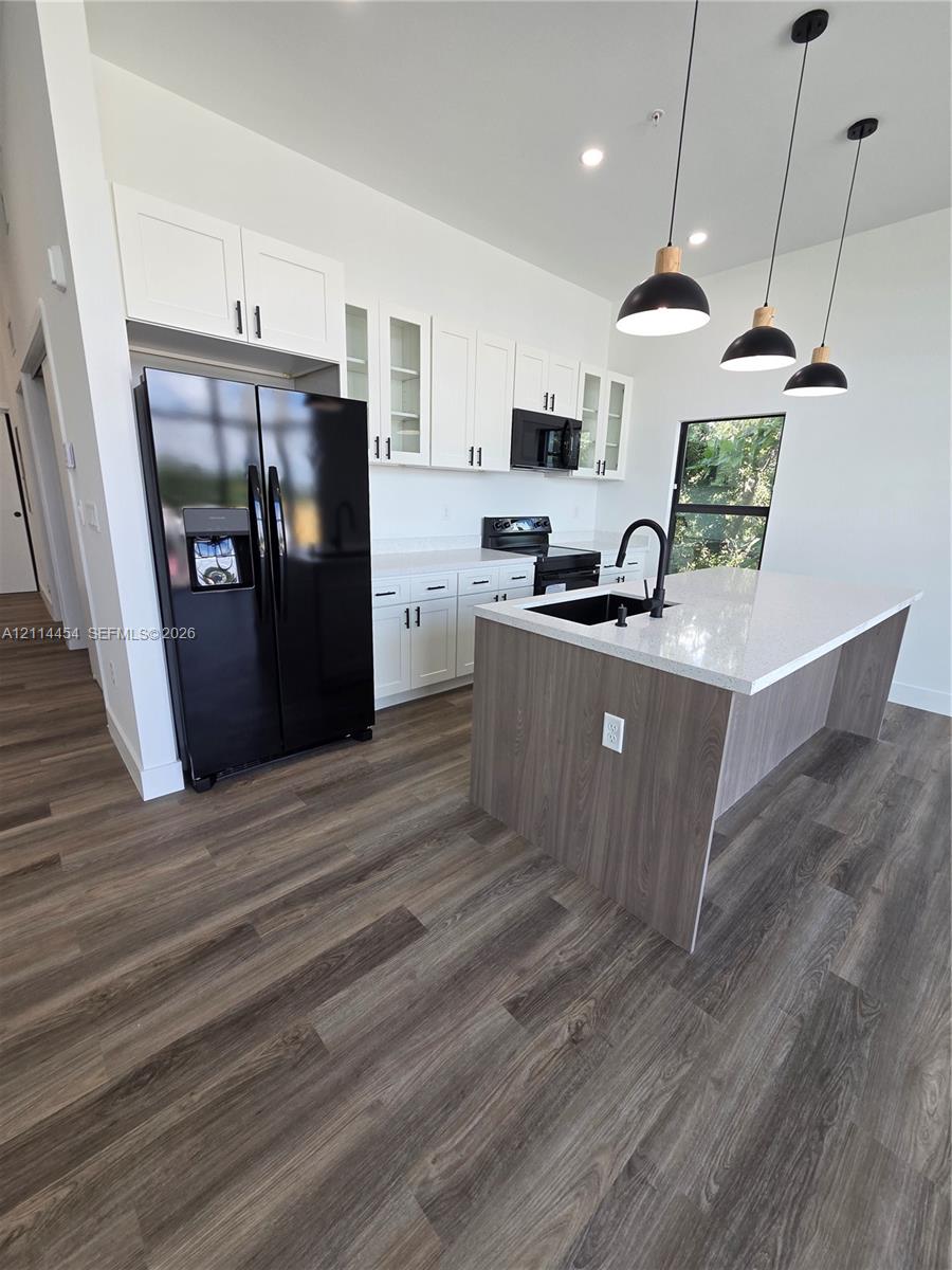 Kitchen featuring white cabinetry, wood-finish flooring, a central island with a quartz countertop, black hardware, and three pendant lights