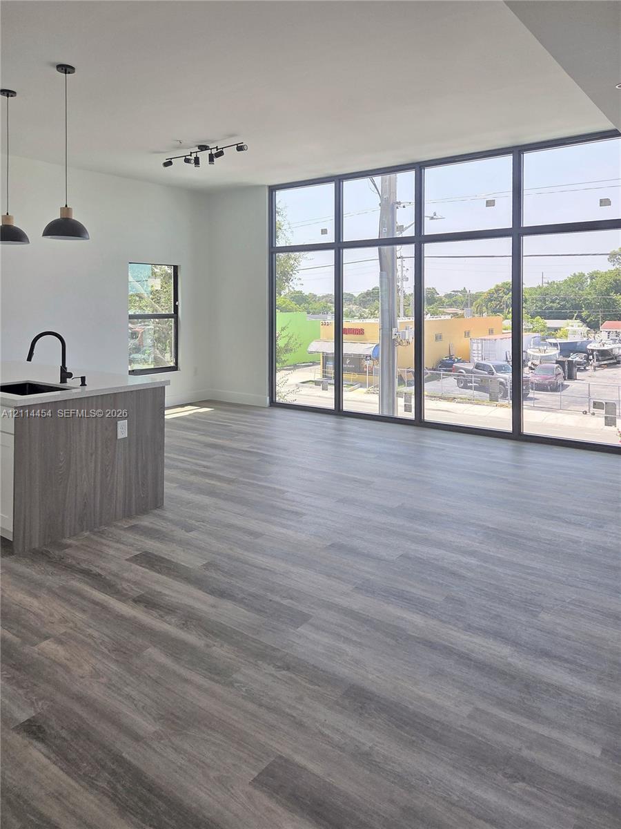 Open-concept interior featuring floor-to-ceiling windows, wood-finish flooring, a kitchen island with a quartz countertop, and black matte pendant lighting