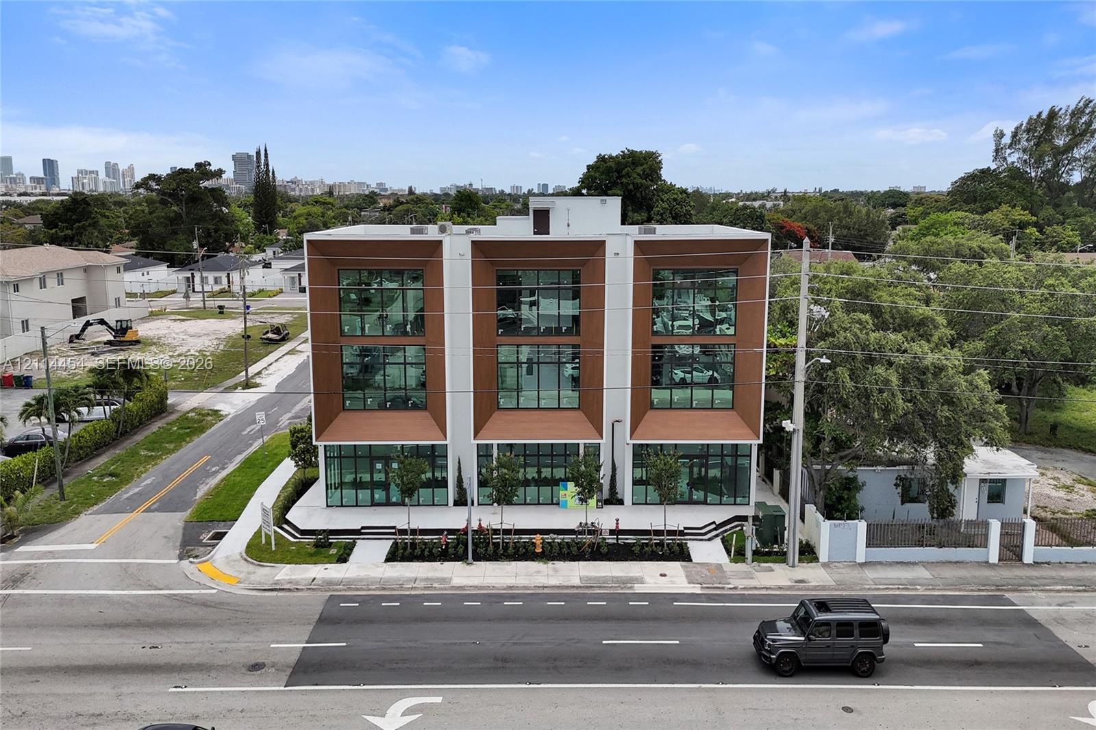 Modern three-story commercial facade featuring expansive floor-to-ceiling glass windows, recessed metallic-finish paneling, and a landscaped concrete exterior plaza