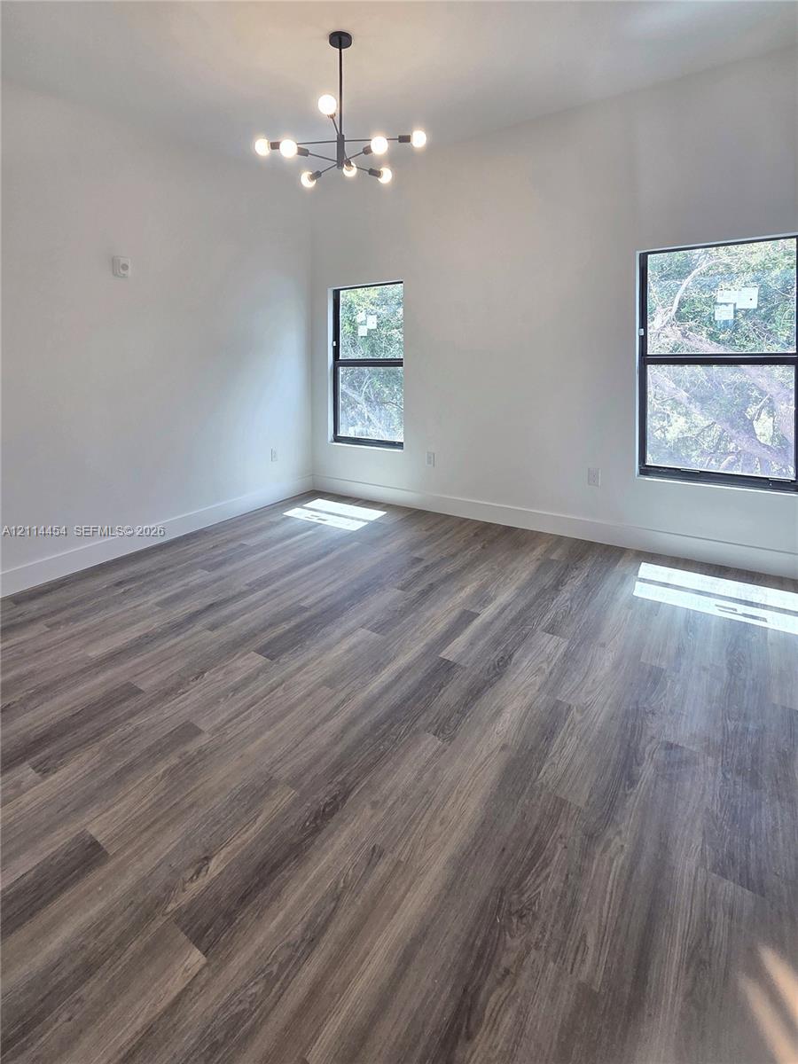 Interior space featuring wood-finish flooring, high ceilings, large windows with dark frames, and a multi-arm modern chandelier