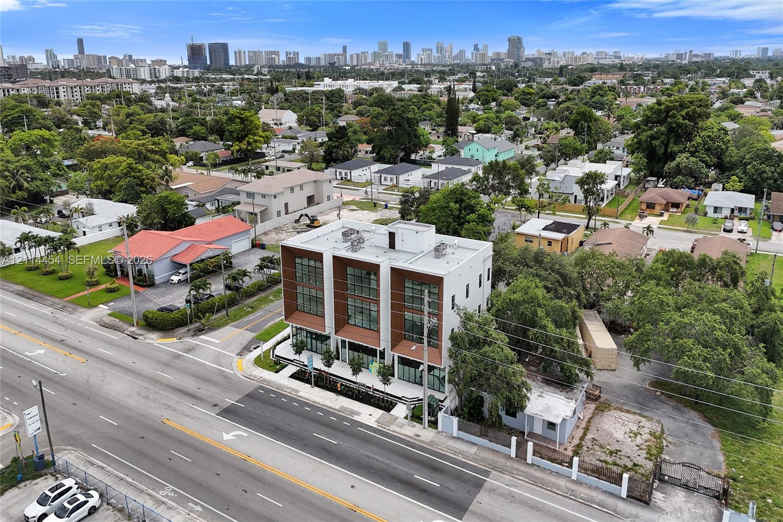 Contemporary three-story structure featuring a concrete facade, wood-finish paneling, expansive floor-to-ceiling windows, a flat roof, and metal balcony railings