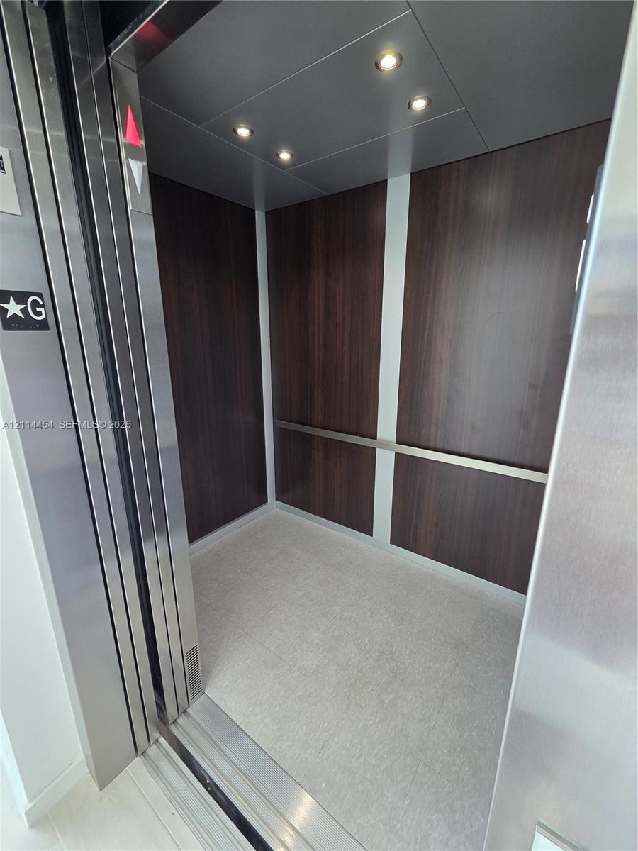 Private elevator featuring stainless steel door frames, rich wood-finish wall paneling, integrated recessed ceiling lighting, and a horizontal metal handrail