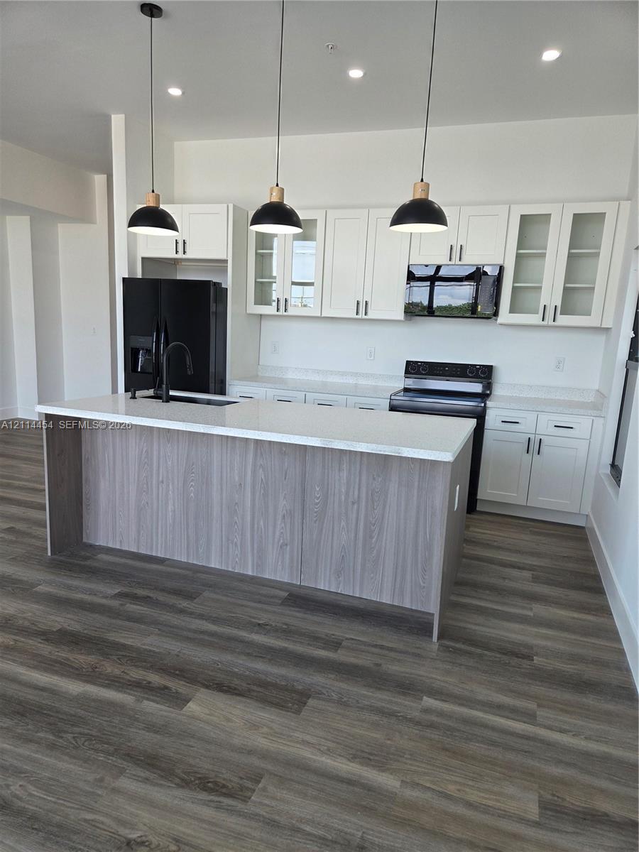 Kitchen featuring white Shaker-style cabinetry, a central island with wood-finish paneling, quartz countertops, black pendant lighting, and wood-finish flooring
