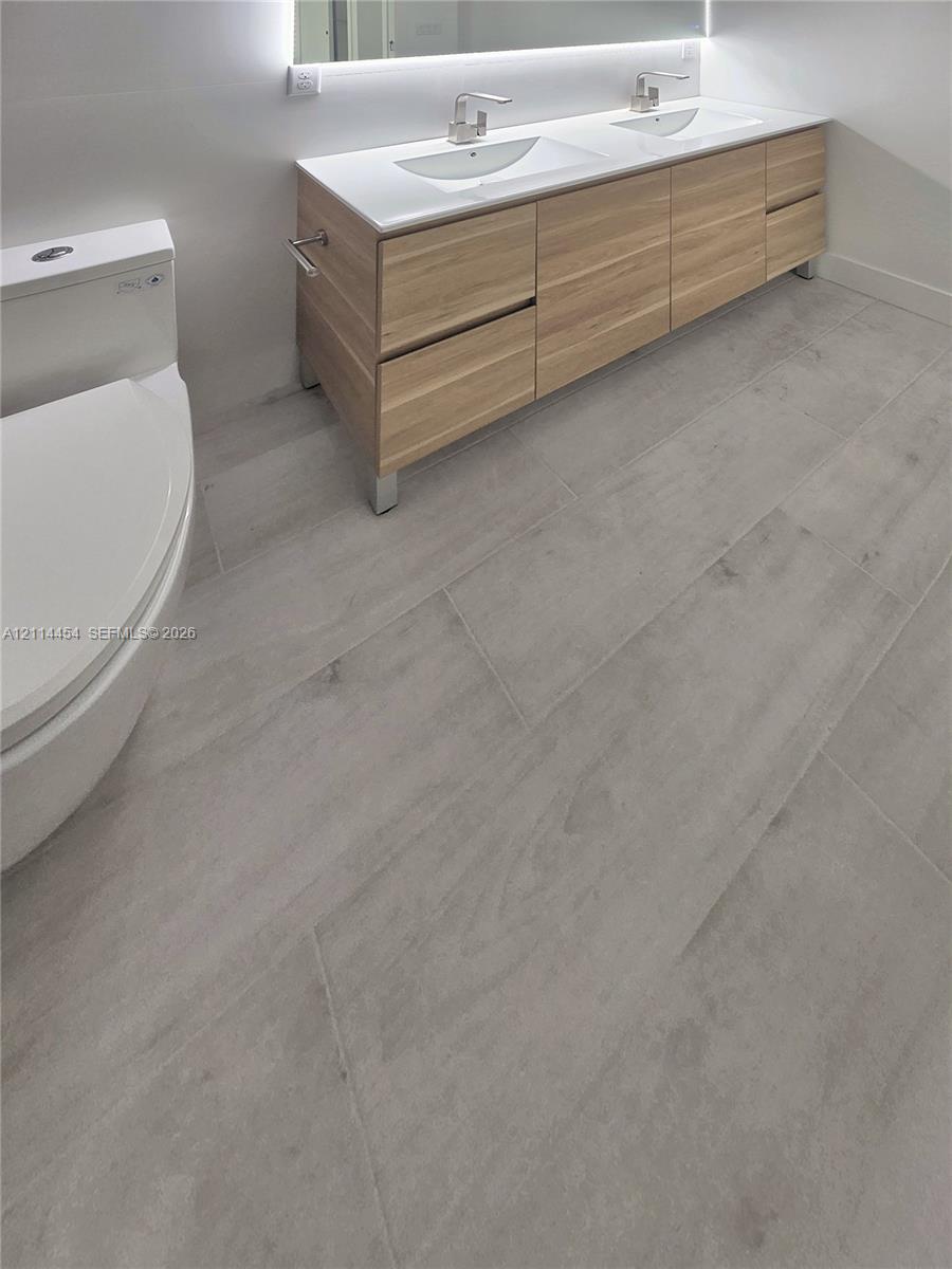Modern floating vanity featuring light-toned cabinetry, dual rectangular under-mount sinks, integrated lighting, and neutral large-format tile flooring