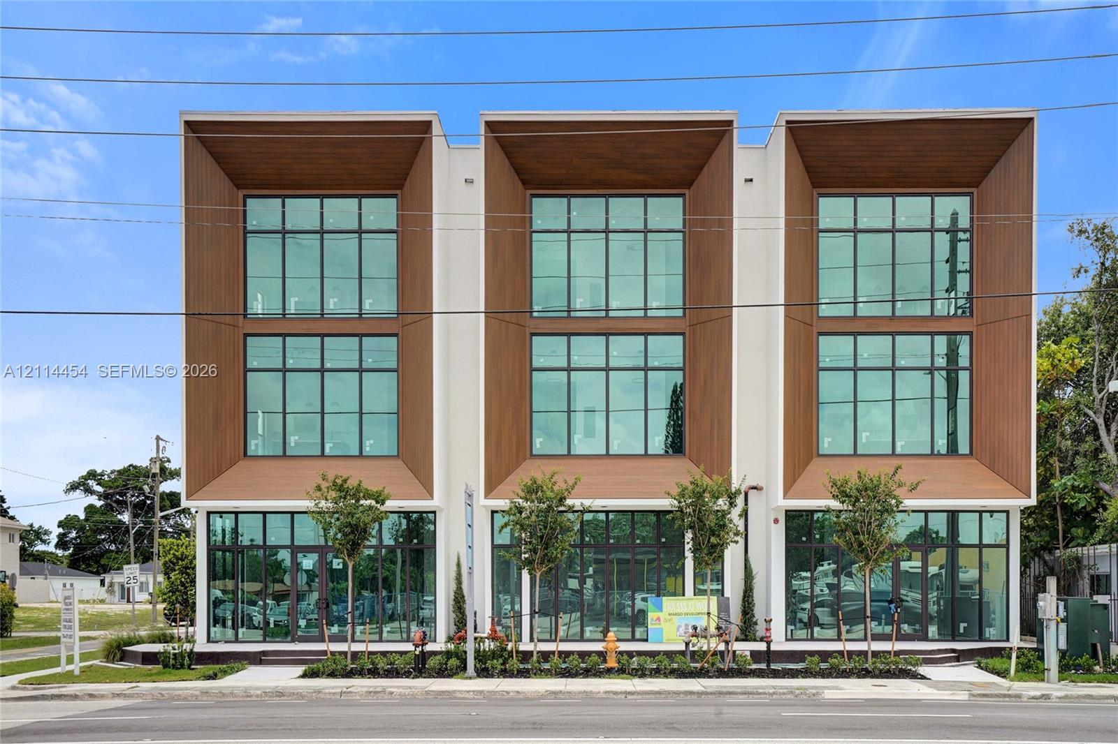 Contemporary three-story structure featuring a smooth stucco exterior, wood-finish paneling, floor-to-ceiling glass windows, and metal-framed storefront entries