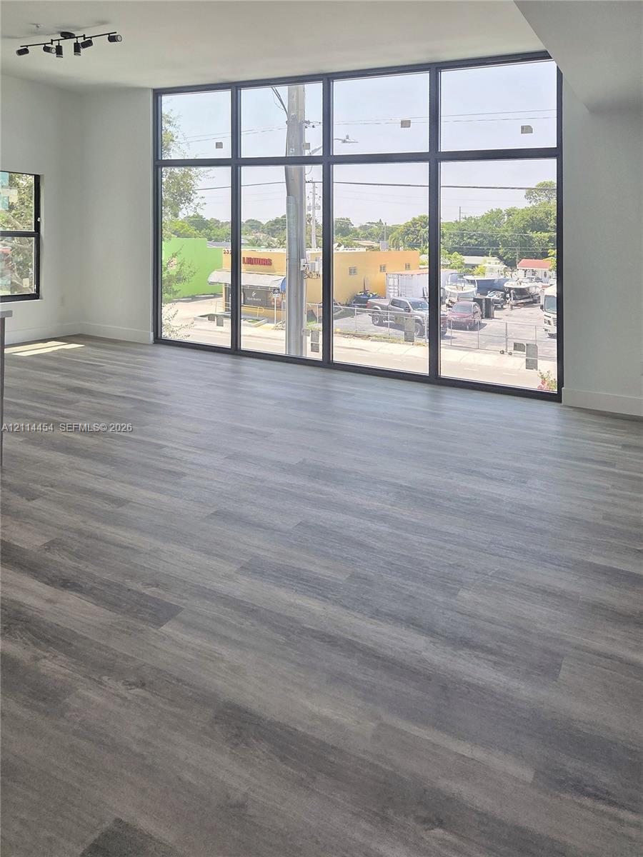 Floor-to-ceiling windows with black frames, wood-finish flooring, and black multi-directional track lighting