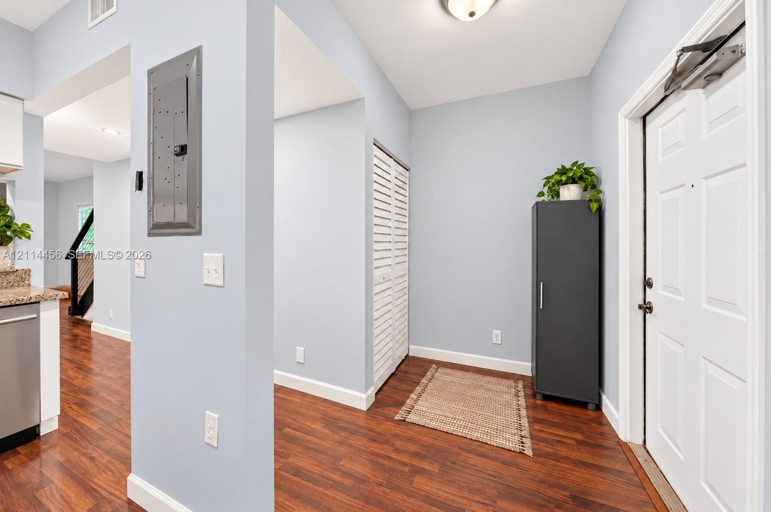 Entryway featuring wood-finish flooring, white paneled entry door with hardware, and white louvered closet doors