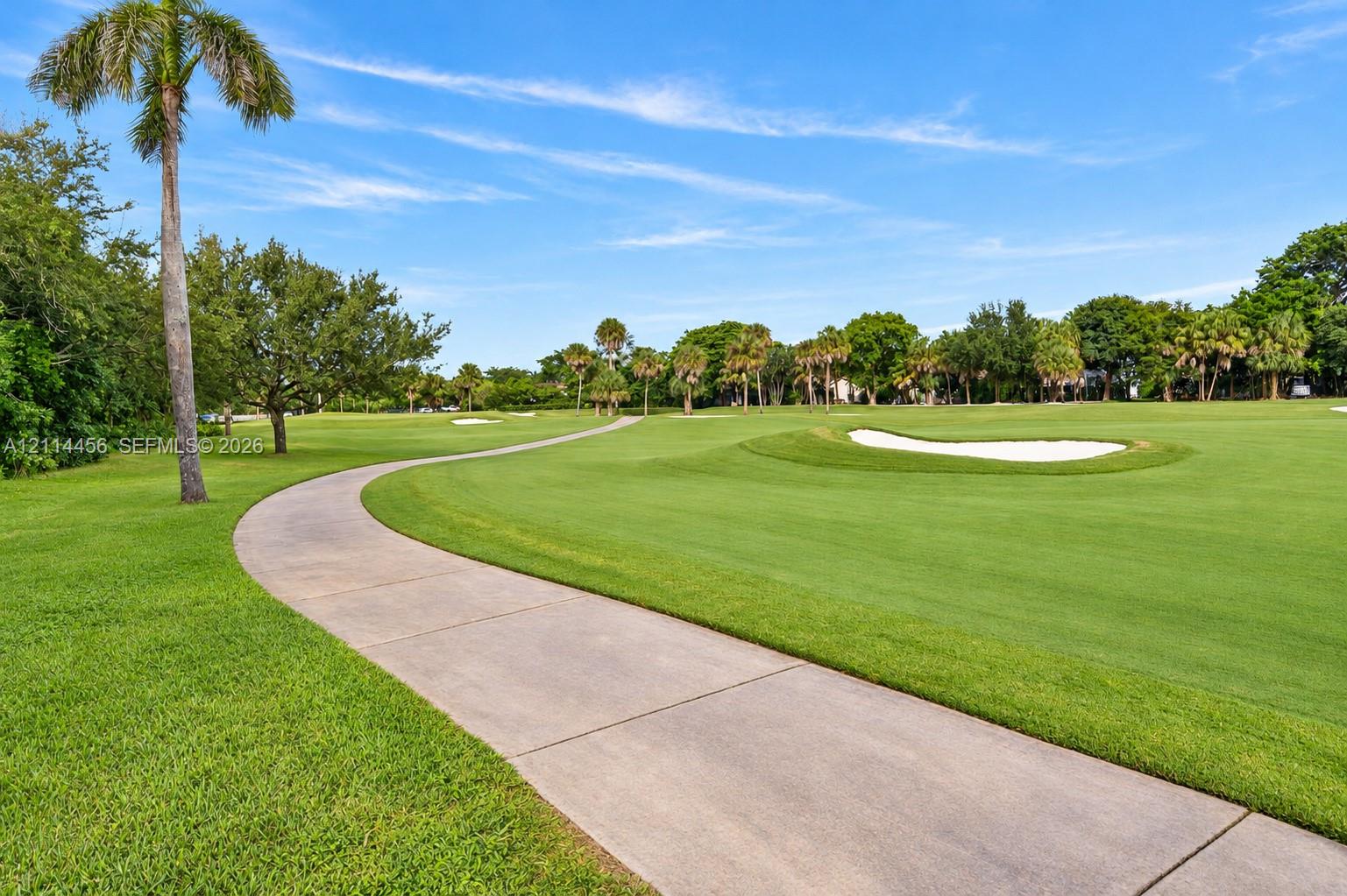 Expansive manicured lawn featuring a paved concrete pathway, sand bunkers, and mature palm trees