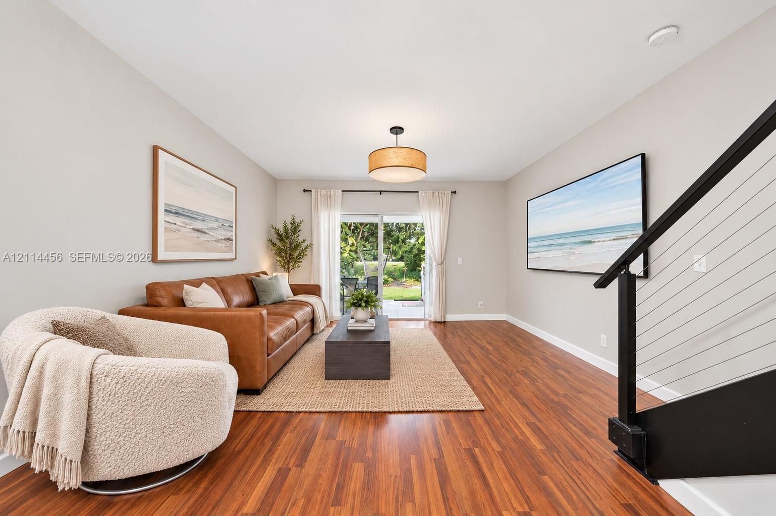 Living area featuring wood-finish flooring, a drum pendant light fixture, sliding glass doors, and a staircase with a black metal handrail and horizontal cable railing