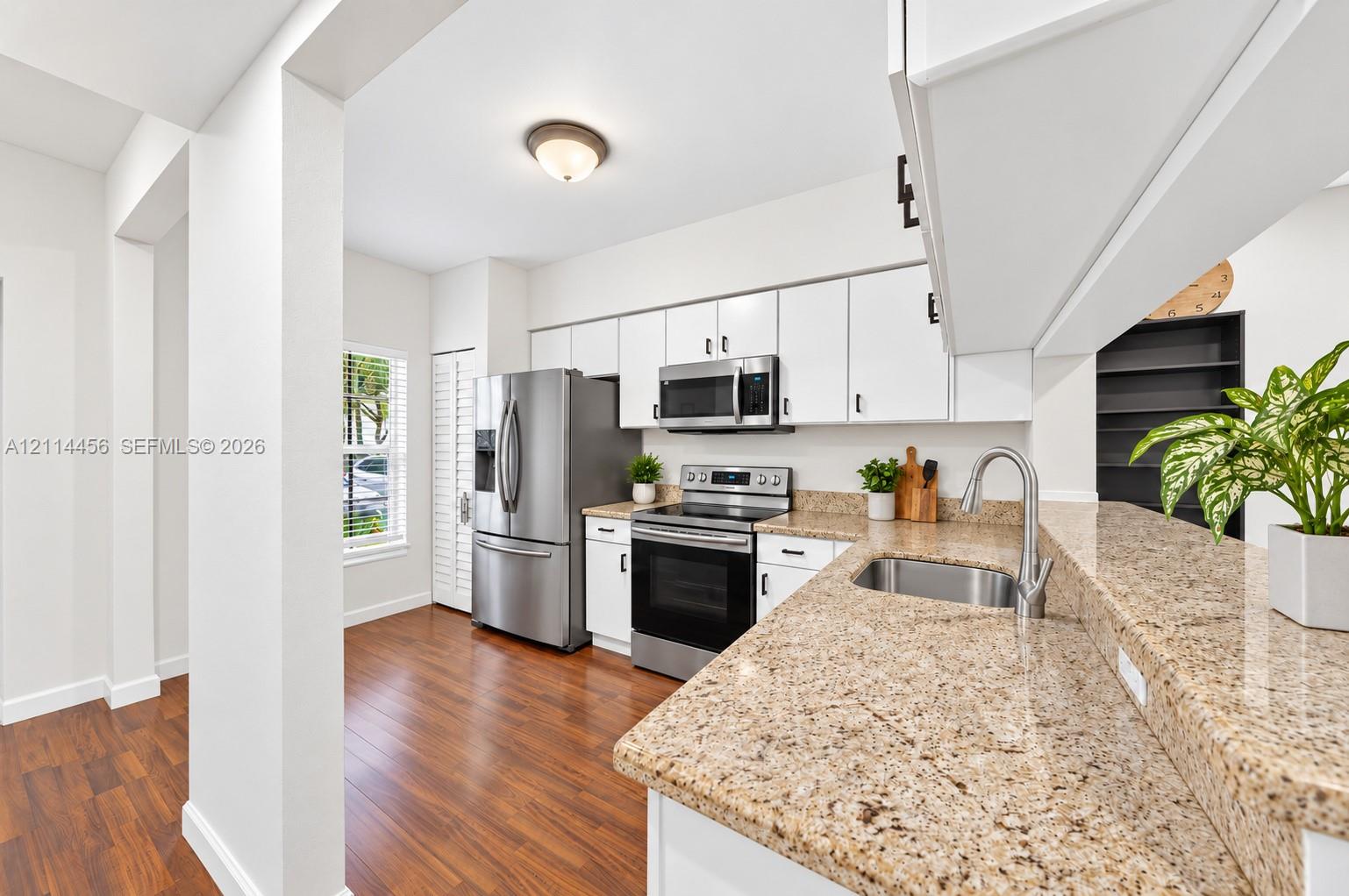 Kitchen featuring white cabinetry, stone countertops, stainless steel appliances, a double-basin sink, and wood-finish flooring